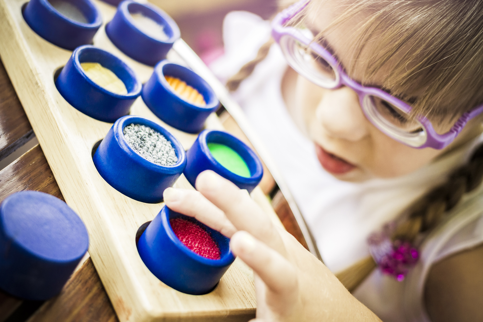 Cute child with poor vision is touching the wooden tactile rolls of different texture and colour as a part of educational therapy. AdobeRGB profile.