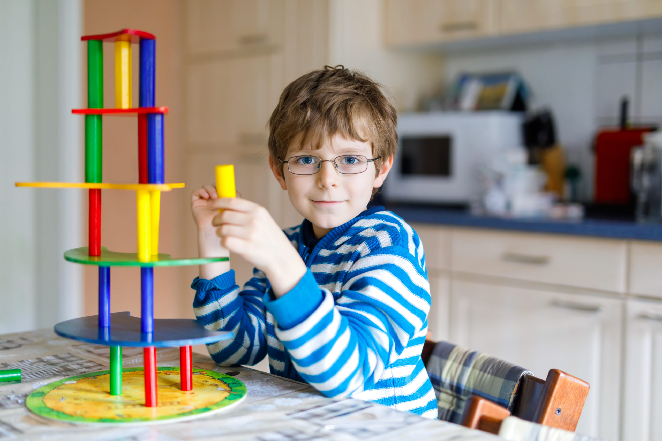 Blond child with glasses playing with lots of colorful wooden blocks game indoor. Active funny kid boy having fun with building and creating, balance toy. Kindergarten. Home, kidsroom. Cognitive development